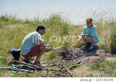 Caucasian couple roasting sausages over a fire. Caucasian couple roasting sausages over a fire. 132510149