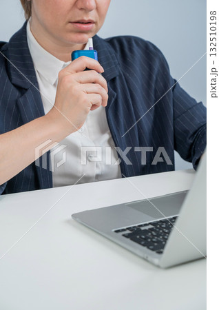 Business woman smoking an electronic cigarette while working on a laptop. Tobacco heating system. 132510198