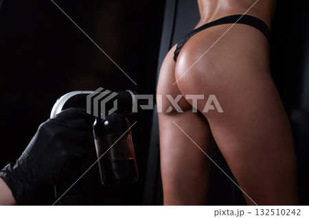 The master applies tinting paint on the back of a woman. Instant tanning treatment. 132510242