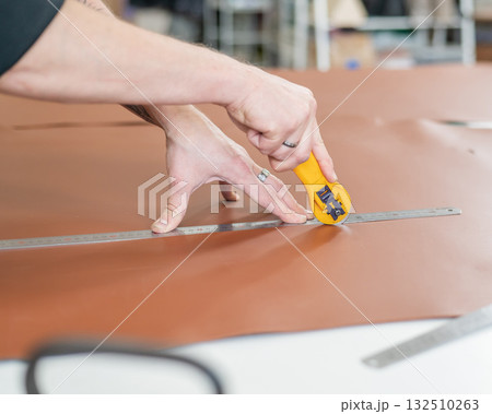 Leatherworker measuring and cutting leather in workshop.  132510263