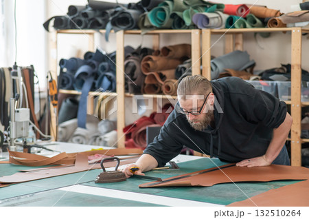Caucasian bearded man working as a tanner in a workshop. Caucasian bearded man working as a tanner in a workshop. 132510264