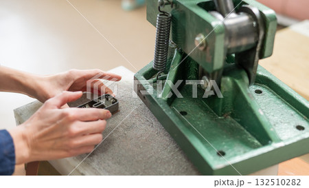 A woman makes holes in a leather belt in a workshop. 132510282