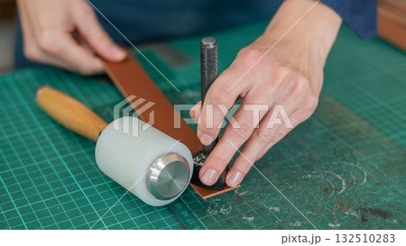 Woman tanner processes the edges of a leather belt in a workshop.  132510283
