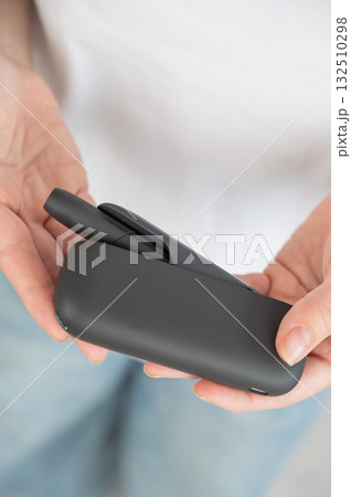 A woman takes a tobacco heating system out of a charger. Electronic cigarette. 132510298