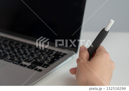 A woman smokes an electronic cigarette while working on a laptop. Tobacco heating system. A woman smokes an electronic cigarette while working on a laptop. Tobacco heating system. 132510299