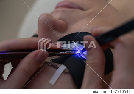 A woman undergoing eyelash extension procedure using an ultraviolet lamp. 132510541