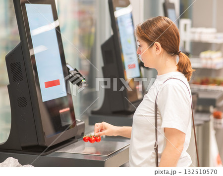A woman weighs cherry tomatoes at a self-service checkout.  132510570
