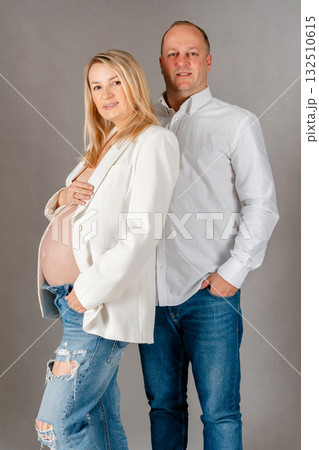 Elegant studio portrait of an expectant couple, woman in white blazer cradling her bump, partner standing close behind in supportive pose, refined, warm composition Elegant studio portrait of an expectant couple, woman in white blazer cradling her bump, partner standing close behind in supportive pose, refined, warm composition 132510615
