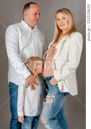 Family portrait of pregnant woman with husband and son, showing love and anticipation for the new baby. Studio shot in white outfits Family portrait of pregnant woman with husband and son, showing love and anticipation for the new baby. Studio shot in white outfits 132510620