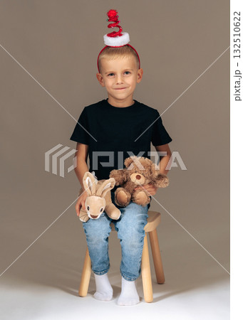 Cute boy wearing Christmas hat, holding teddy bears. Studio holiday portrait of childhood joy and warmth Cute boy wearing Christmas hat, holding teddy bears. Studio holiday portrait of childhood joy and warmth 132510622