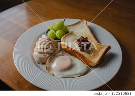 トーストと目玉焼き、鶏ハムとシャインマスカットを添えた洋風の朝食 132510681