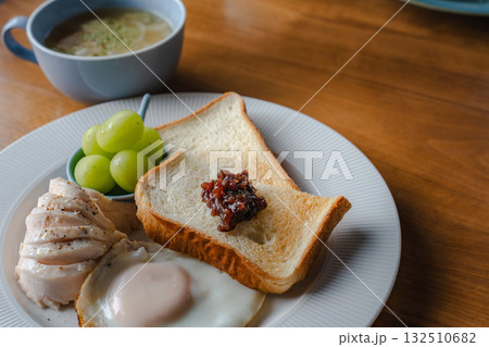 トーストと目玉焼き、鶏ハムとシャインマスカットを添えた洋風の朝食 132510682
