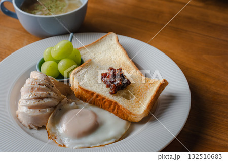トーストと目玉焼き、鶏ハムとシャインマスカットを添えた洋風の朝食 トーストと目玉焼き、鶏ハムとシャインマスカットを添えた洋風の朝食 132510683