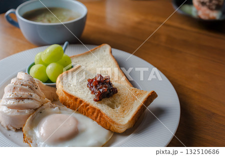 トーストと目玉焼き、鶏ハムとシャインマスカットを添えた洋風の朝食 トーストと目玉焼き、鶏ハムとシャインマスカットを添えた洋風の朝食 132510686