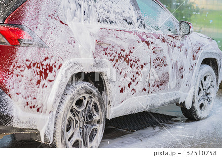 Red SUV with Foam Close-up. Red SUV being cleaned with thick white foam at automatic car wash service during daylight. Concept of vehicle cleaning, auto care, professional detailing Red SUV with Foam Close-up. Red SUV being cleaned with thick white foam at automatic car wash service during daylight. Concept of vehicle cleaning, auto care, professional detailing 132510758