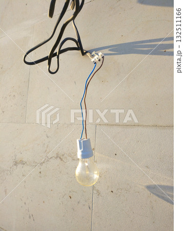 The light bulb hangs against a light concrete wall, illuminated by sunlight 132511166