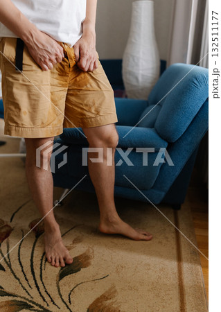 Vertical cropped shot of unhealthy young man grappling with urinary incontinence, anxiously clutching wet pants as navigates discomfort and embarrassment of situation. Concept of healthy lifestyle. Vertical cropped shot of unhealthy young man grappling with urinary incontinence, anxiously clutching wet pants as navigates discomfort and embarrassment of situation. Concept of healthy lifestyle. 132511177