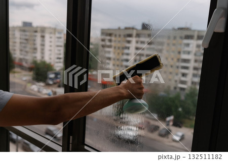 Close-up cropped shot of unrecognizable washing large window overlooking city street, using professional squeegee, ensuring streak-free and sparkling clean finish in home environment. 132511182