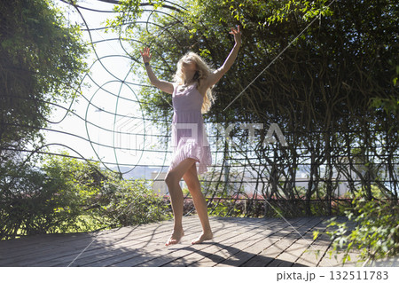 Young woman dancing freely in green outdoor pergola 132511783