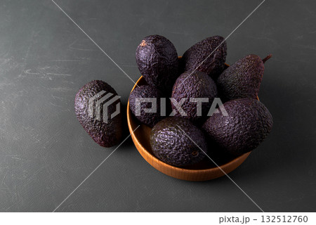Dark, ripe avocados in wooden bowl on a rustic green surface. Dark, ripe avocados in wooden bowl on a rustic green surface. 132512760