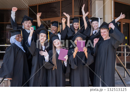 Happy students of different nationalities in graduation gowns hold their diplomas. 132513125