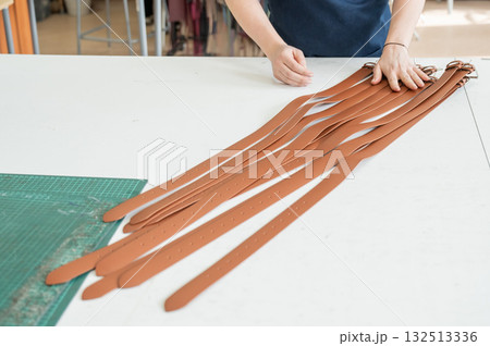 Caucasian woman makes belts from genuine leather in a workshop. Caucasian woman makes belts from genuine leather in a workshop. 132513336