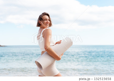 Smiling young woman with rolled yoga mat standing Smiling young woman with rolled yoga mat standing 132515658