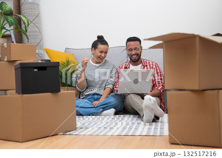happy Young couple, surrounded by boxes in new apartment, uses laptop for online decor shopping, crafting their dream space, or organizing their move happy Young couple, surrounded by boxes in new apartment, uses laptop for online decor shopping, crafting their dream space, or organizing their move 132517216
