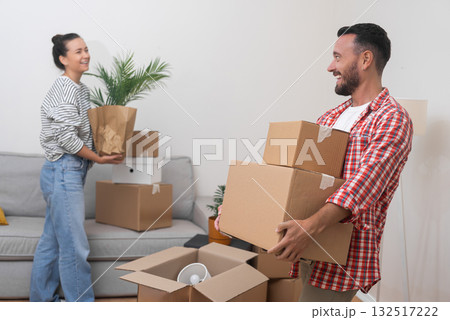 Welcome Home Abroad: A happy couple, after moving abroad, enters the living room with a pile of cardboard boxes from their relocation service, welcoming the sense of belonging Welcome Home Abroad: A happy couple, after moving abroad, enters the living room with a pile of cardboard boxes from their relocation service, welcoming the sense of belonging 132517222