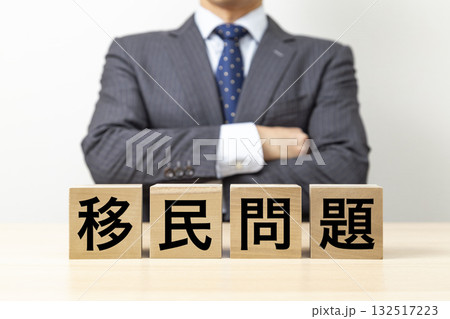 「移民問題」と書かれたブロックと腕組みをするビジネスマン 「移民問題」と書かれたブロックと腕組みをするビジネスマン 132517223