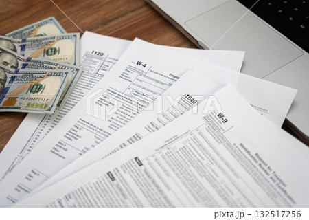 Tax forms and dollar bills on a wooden desk with a laptop. Financial management, tax refund, and accounting concept.  132517256