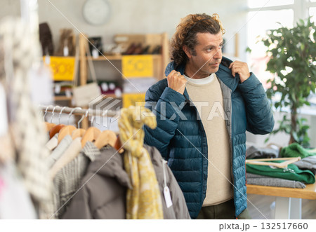 Man try on down jacket in front of mirror in clothes store Man try on down jacket in front of mirror in clothes store 132517660
