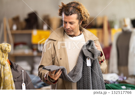 Handsome positive man client selecting new sweaters for cold season in clothing shop 132517766
