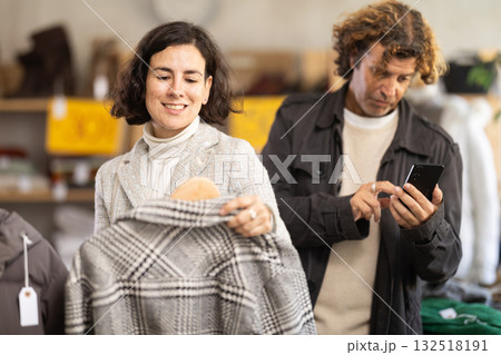 Woman choosing jackets and coats next to man with phone 132518191