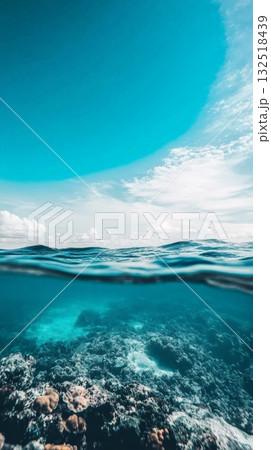 Crystal clear turquoise water reveals a vibrant coral reef below the surface, while above, gentle waves roll under a partially cloudy sky, creating a serene and captivating seascape 132518439