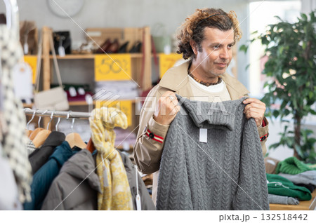 man stands near the counter with clothes and chooses a sweater 132518442