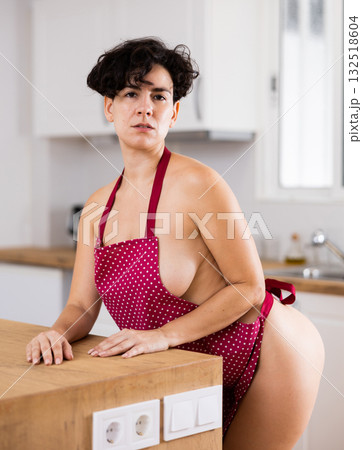 Naked woman in apron posing in kitchen Naked woman in apron posing in kitchen 132518604