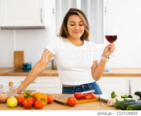 Portrait of woman with glass of red wine in modern kitchen - housewife prepares a vegetable salad and drinks red wine Portrait of woman with glass of red wine in modern kitchen - housewife prepares a vegetable salad and drinks red wine 132518929