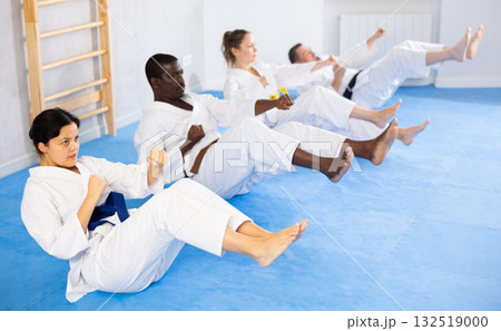 Multinational women and men in kimono train abdominal muscles and do punches at the same time during karate training 132519000