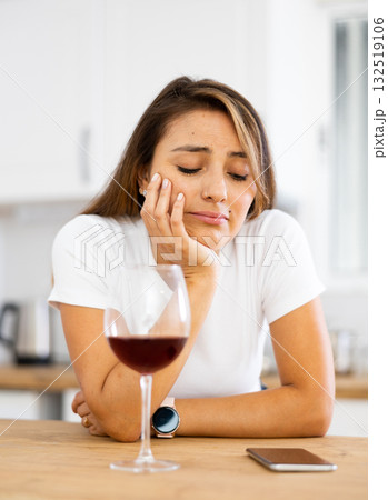 Frustrated young woman drinking wine and waiting for call in home kitchen 132519106