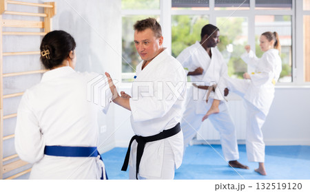 Woman and man in kimono sparring in gym during karate training Woman and man in kimono sparring in gym during karate training 132519120