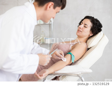 Male anesthesiologist injecting anesthetic into vein on her arm with syringe in cosmetology clinic Male anesthesiologist injecting anesthetic into vein on her arm with syringe in cosmetology clinic 132519129