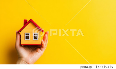 Protecting house model with hands symbolizes real estate investment, insurance, and home buying on a vibrant yellow background with copy space 132519315