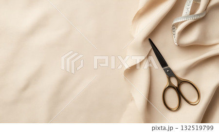 Professional golden scissors and measuring tape are lying on draped beige silk fabric, creating a stylish and elegant flat lay composition for sewing, tailoring, or fashion design concept 132519799