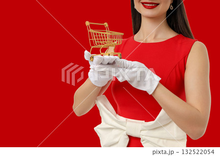 Woman in red dress displays small golden shopping cart 132522054