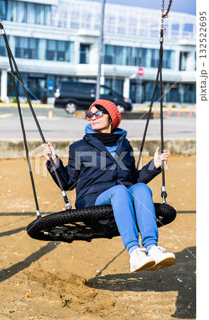 Russian woman about 50 years old swinging on a playground swing at the beach in Primorsky Krai, Russia, enjoying a sunny autumn day with nostalgic mood. Russian woman about 50 years old swinging on a playground swing at the beach in Primorsky Krai, Russia, enjoying a sunny autumn day with nostalgic mood. 132522695