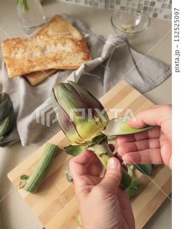 Anonymous person peels artichoke in kitchen at home. Healthy eating and traditional Italian dish. Fresh seasonal farm produce. Anonymous person peels artichoke in kitchen at home. Healthy eating and traditional Italian dish. Fresh seasonal farm produce. 132525097