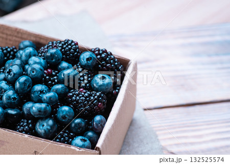 Blueberries and blackberries in a cardboard box on a wooden table Blueberries and blackberries in a cardboard box on a wooden table 132525574