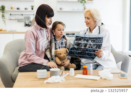 A doctor shows an X-ray to a mother and her child, who is wrapped in a blanket, in a medical consultation setting. 132525957