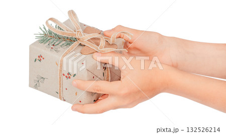 Hands holding a Christmas gift wrapped in eco kraft paper with pine branch, berries, and natural twine, isolated on white background. Sustainable holiday packaging and eco-friendly celebration concept 132526214